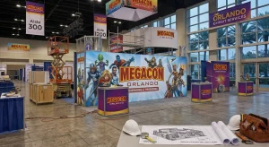 MegaCon Orlando trade show booth with comic art and setup crew visible.